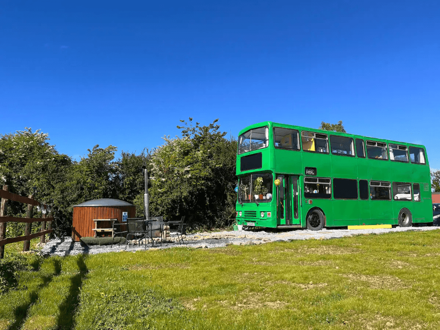 the bus and wood burning hot tub on a gorgeous summers day. Blue sky and green grass.